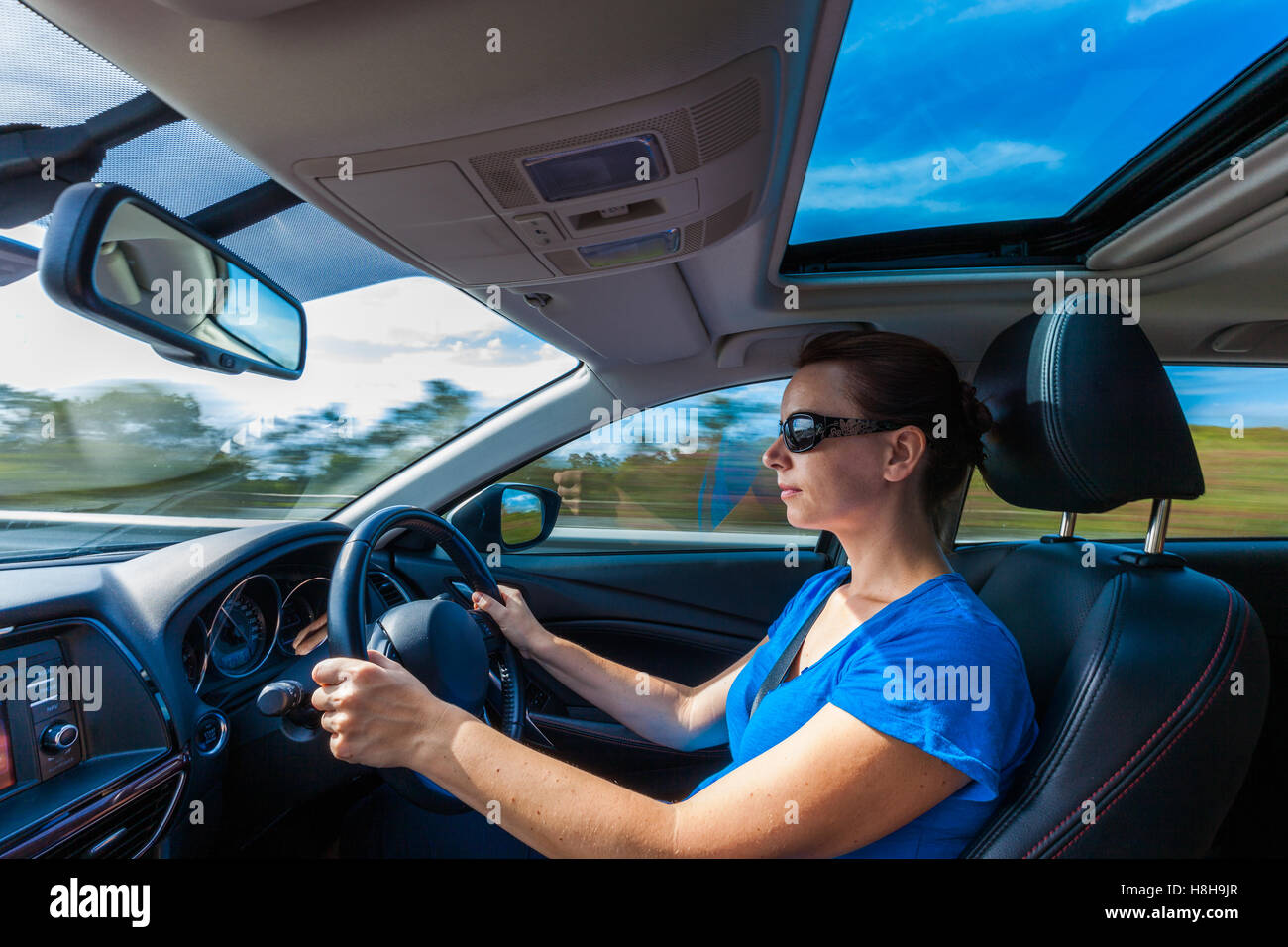 Your woman driving luxurious car with roof window on highway Stock