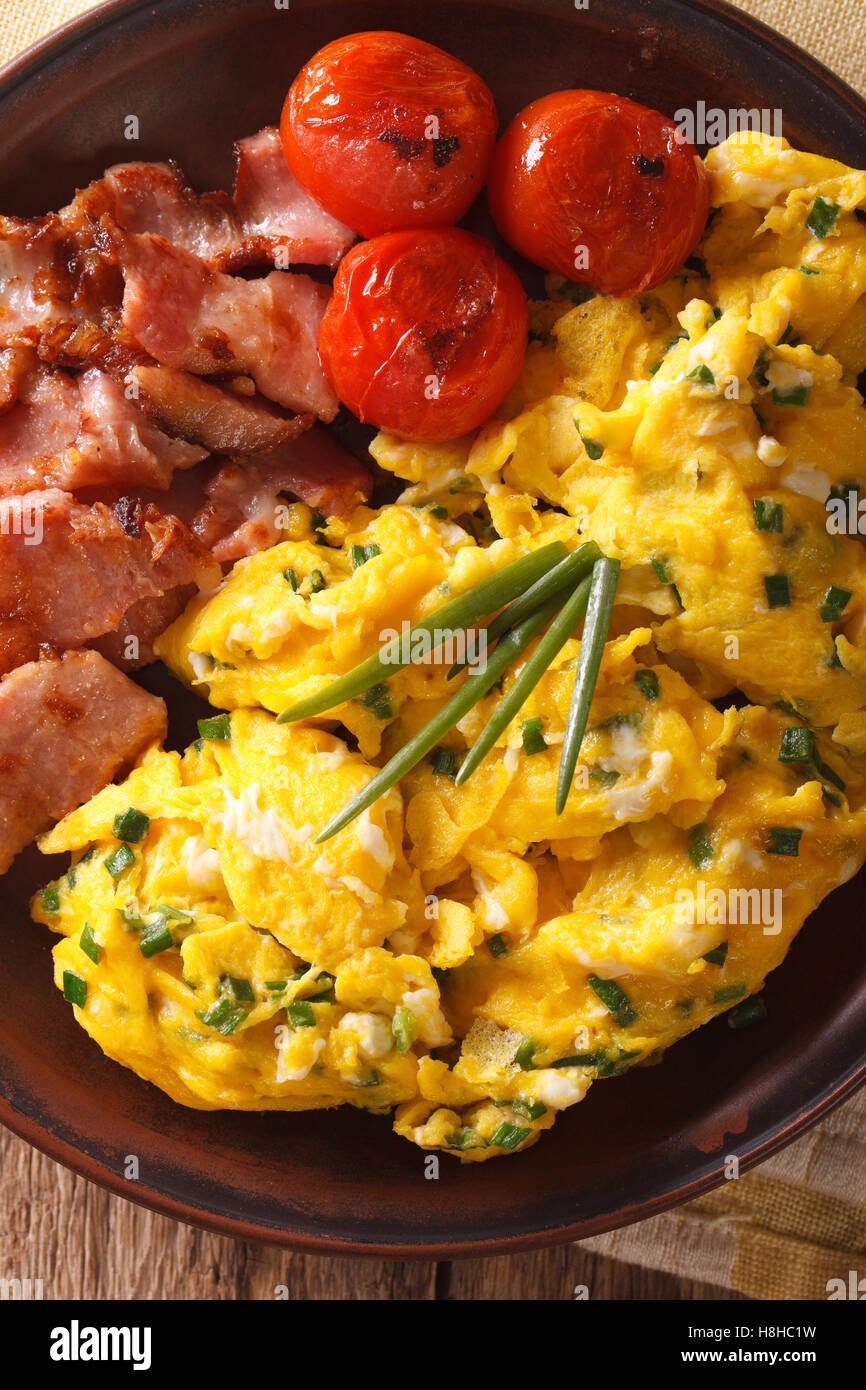 Tasty scrambled eggs and chives, fried bacon on a plate close-up ...