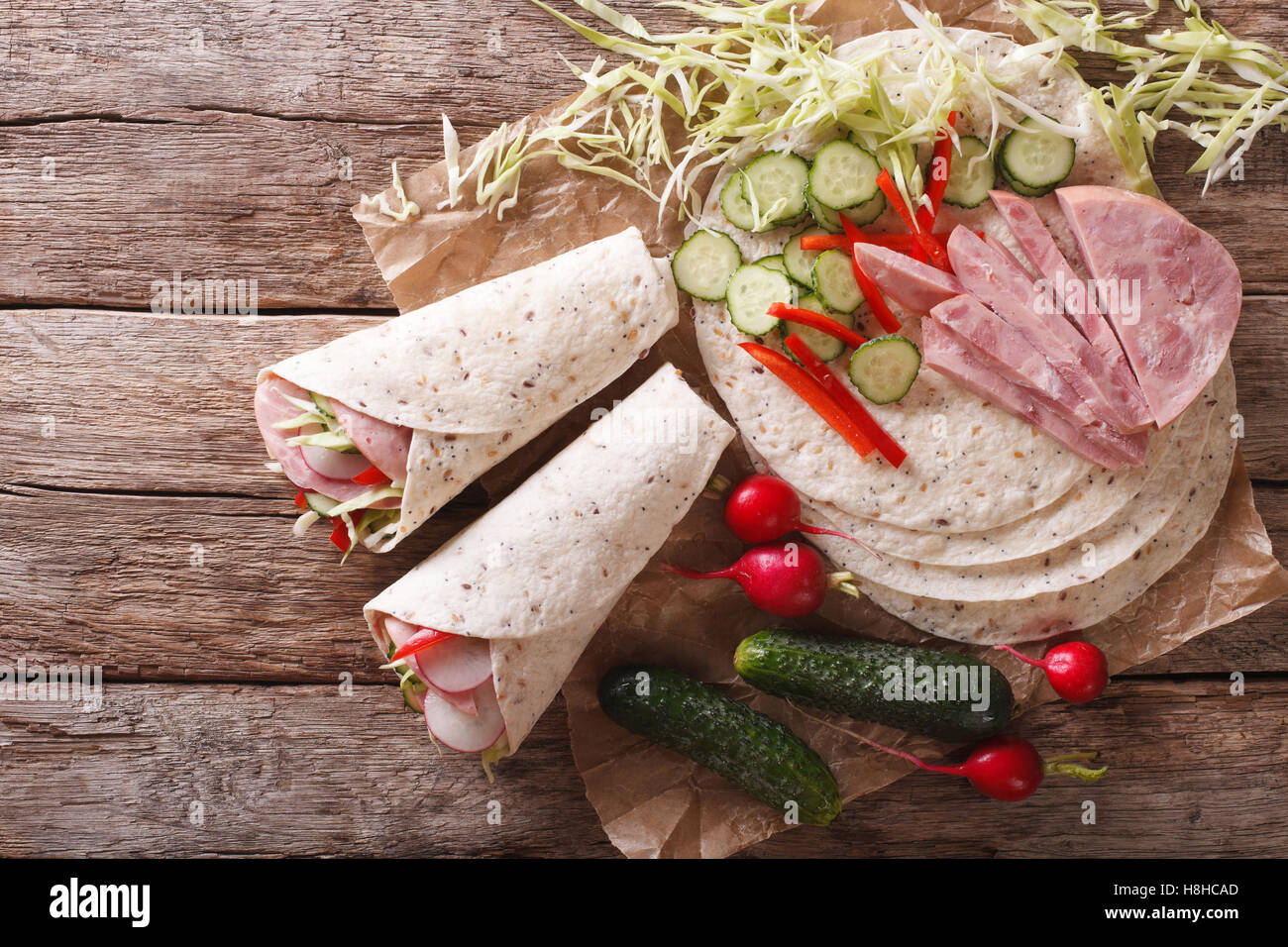 Tortilla Roll with ham and vegetables close-up and ingredients on the table. Horizontal view from above Stock Photo