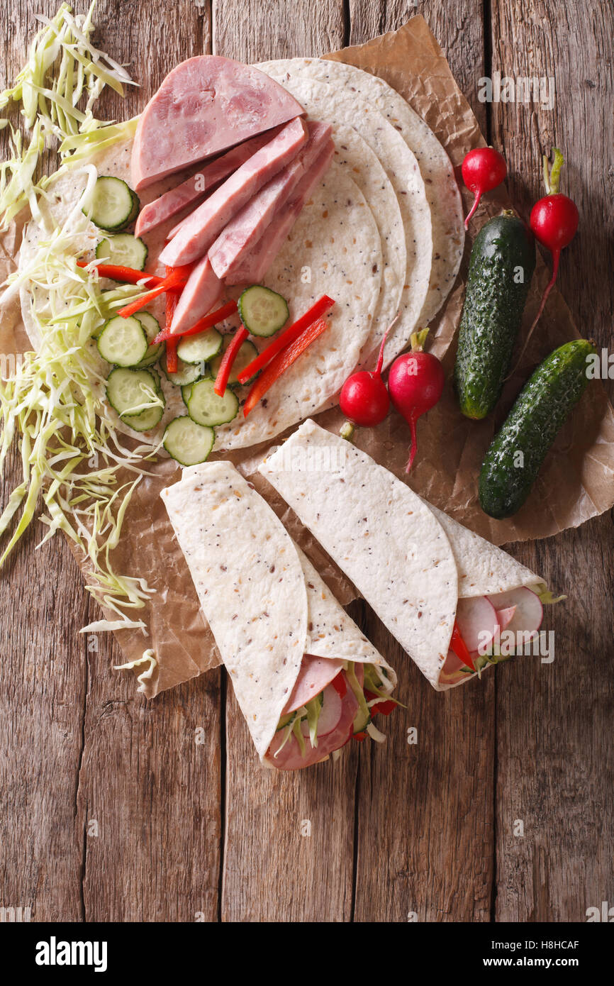 Tortilla Roll with ham and vegetables close-up and ingredients on the table. vertical view from above Stock Photo
