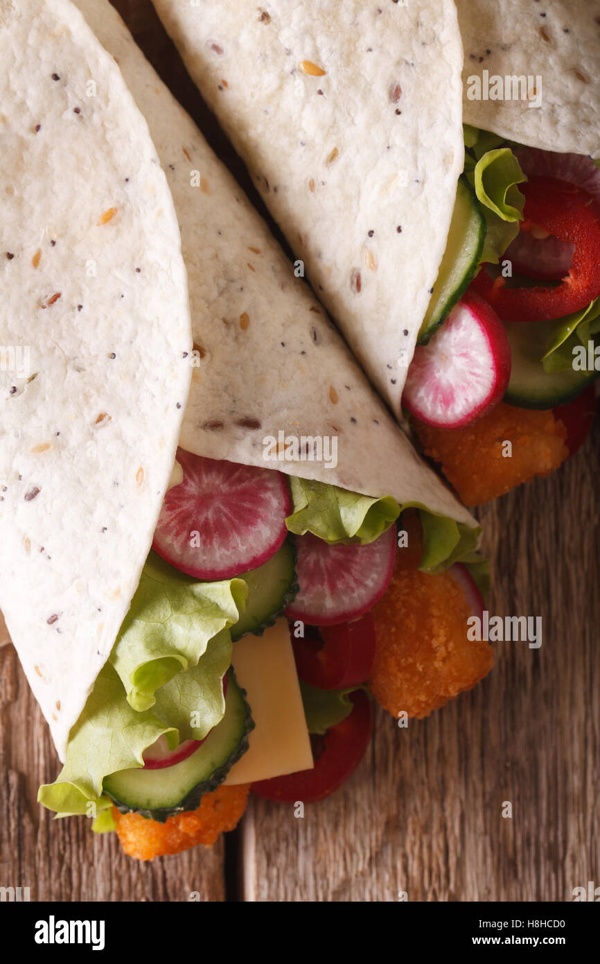 Burrito with fish fingers, and vegetables macro on the table. vertical