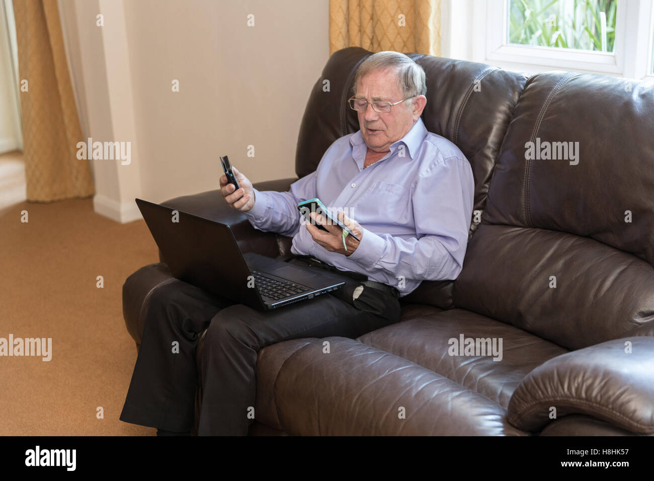 Old age Pensioner trying to use modern electronic devices like laptop and mobile phone. Stock Photo