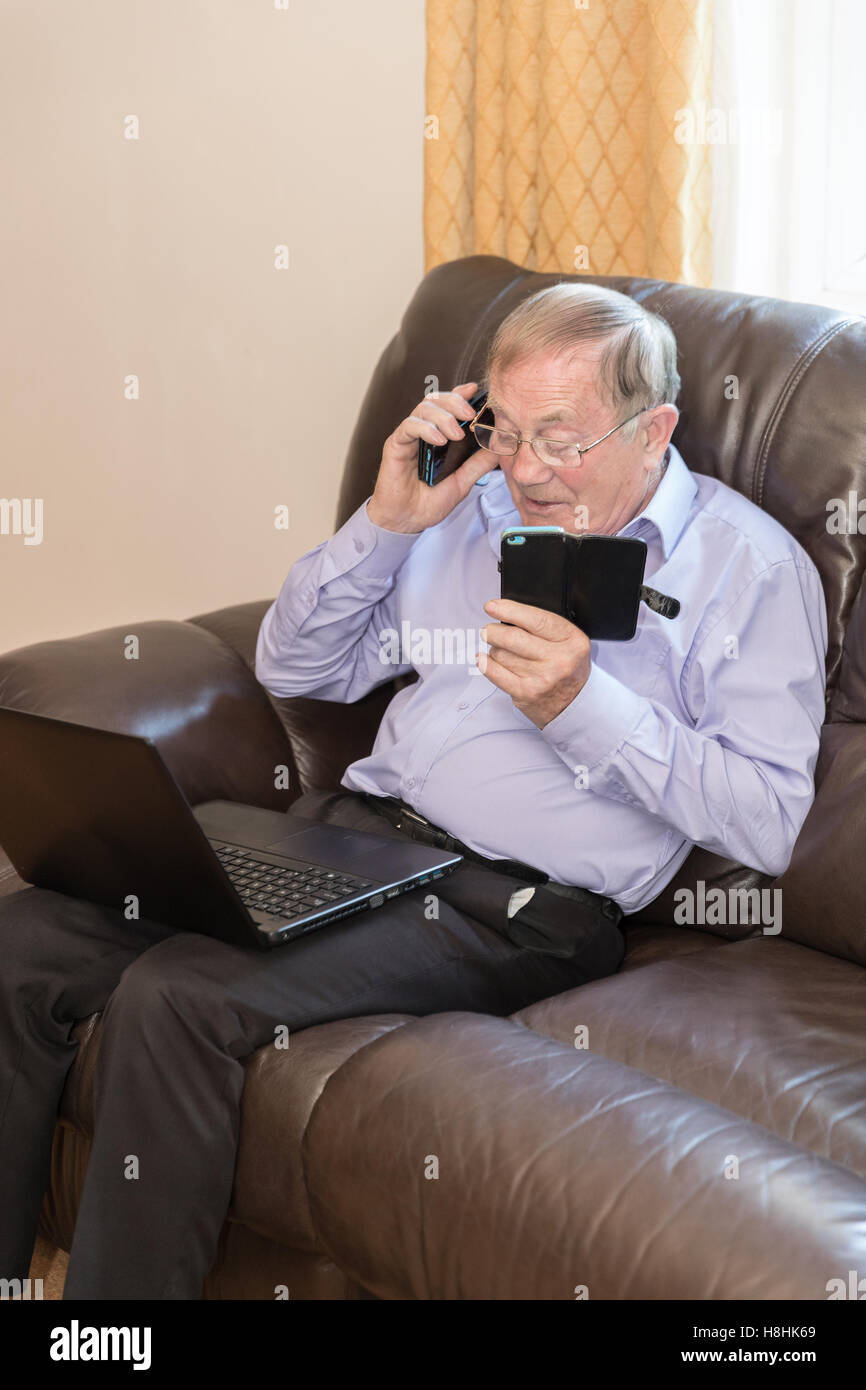 Vertical shot of pensioner using modern electronic devices like laptop and mobile phone Stock Photo