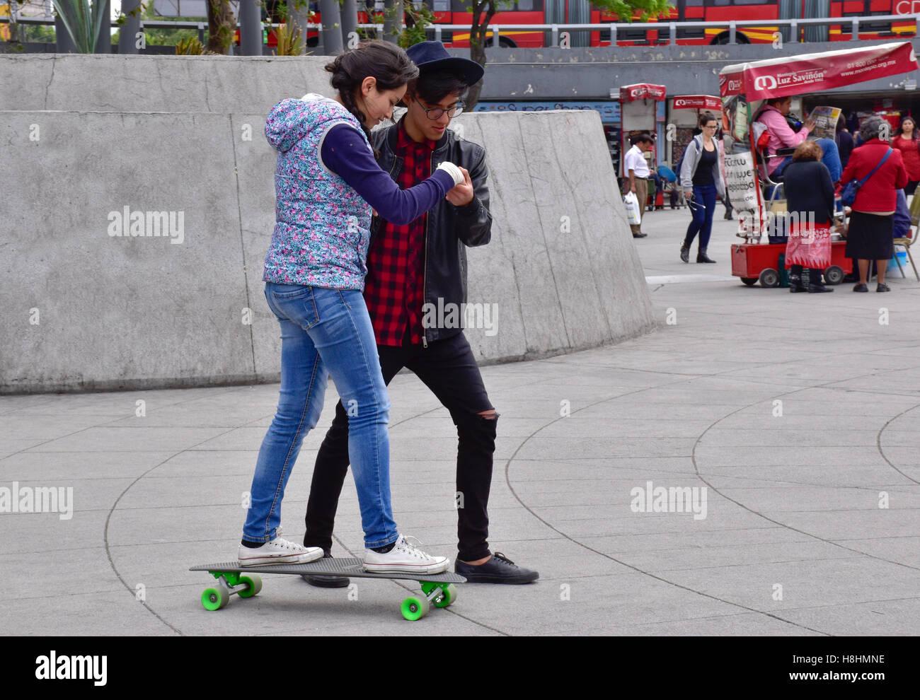 Mexican boy helping girl learn to skateboard, Mexico City, Mexico Stock Photo
