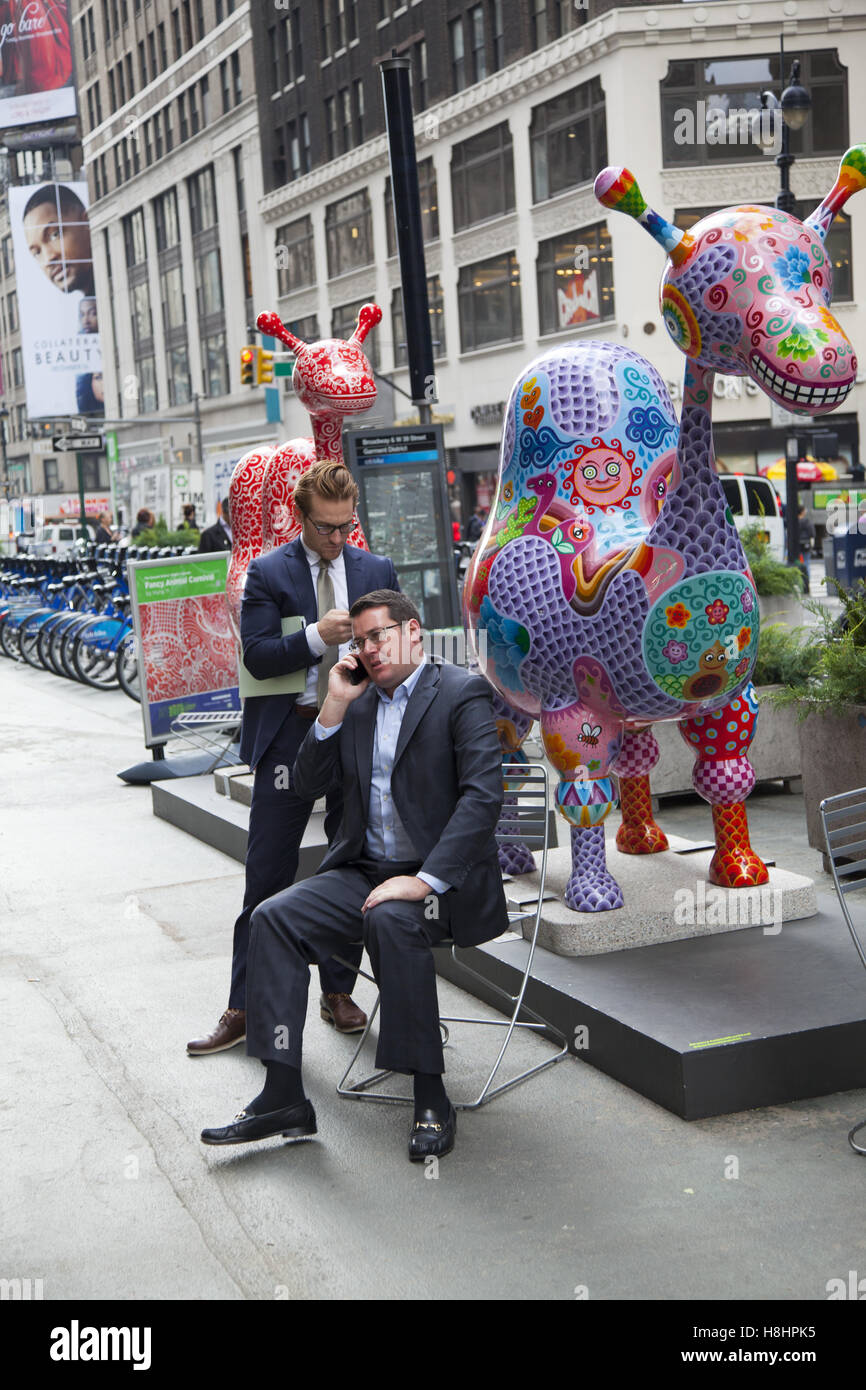 Businessmen sit and use their cell phones along Broadway in the Garment District where Taiwanese artist Hung Yi is having his 'Fancy Animal Carnival' painted sculptures displayed in New York City. Stock Photo