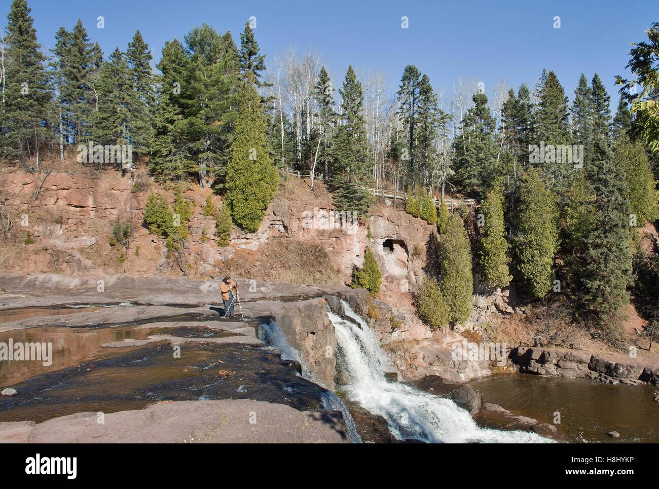A man taking photos while standing at the top of a waterfall at Gooseberry Falls State Park in Two Harbors, Minnesota, USA. Stock Photo