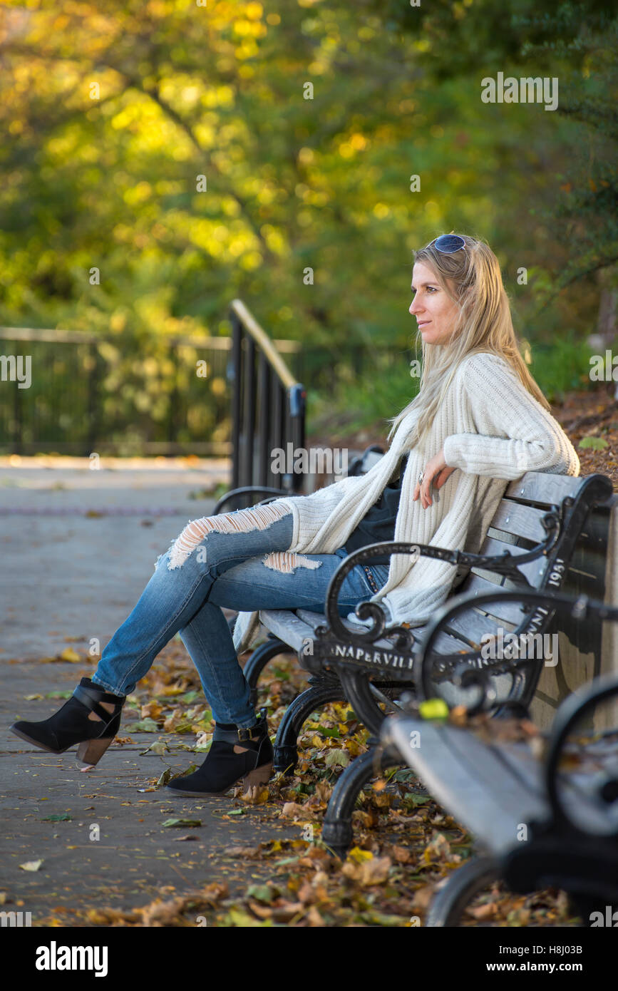 Attractive blond young woman sitting on bench in park with blurred ...
