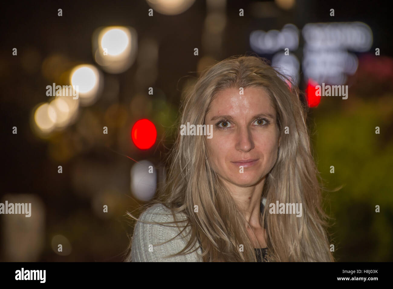 Attractive blonde woman in the city at night with blurred background Stock Photo