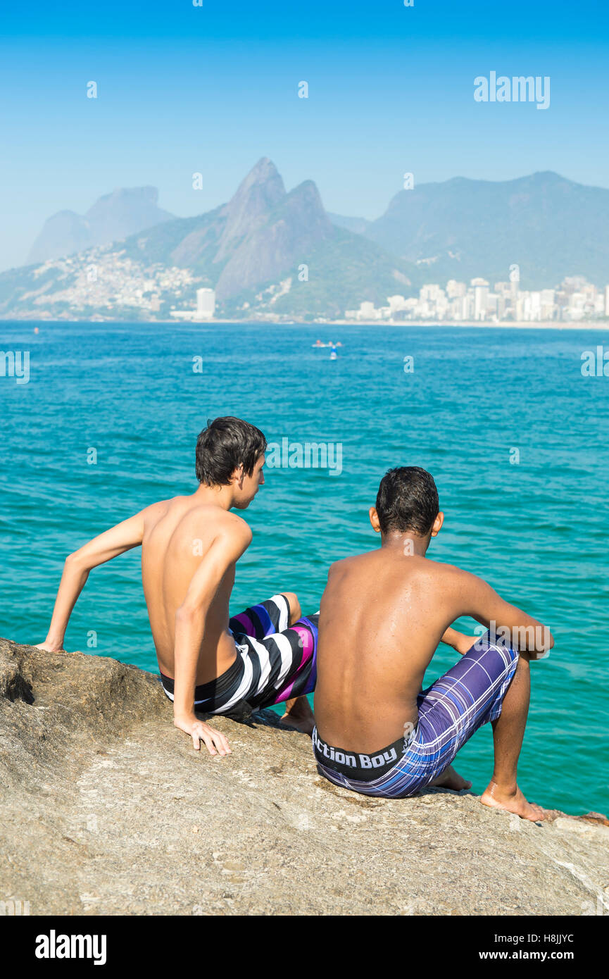 RIO DE JANEIRO - MARCH 27, 2016: Young Brazilians gather to jump from the rocks at Arpoador against a view of Ipanema Beach. Stock Photo