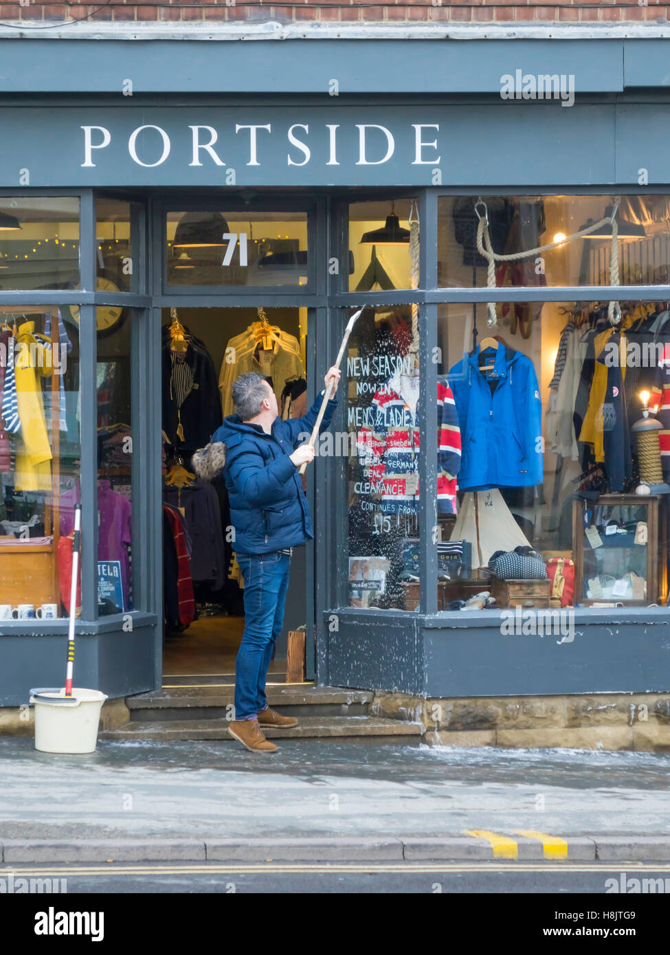 Man with mops and soapy water cleaning windows and paintwork on the front of 'Portside' a Clothing Shop in Whitby Noeth Yorkshir Stock Photo