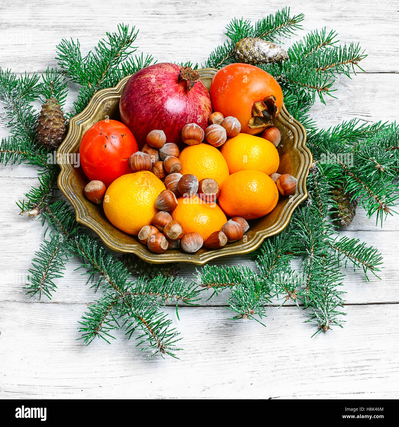 dish with tangerines,pomegranates,persimmons and nuts,decorated with fir branches Stock Photo