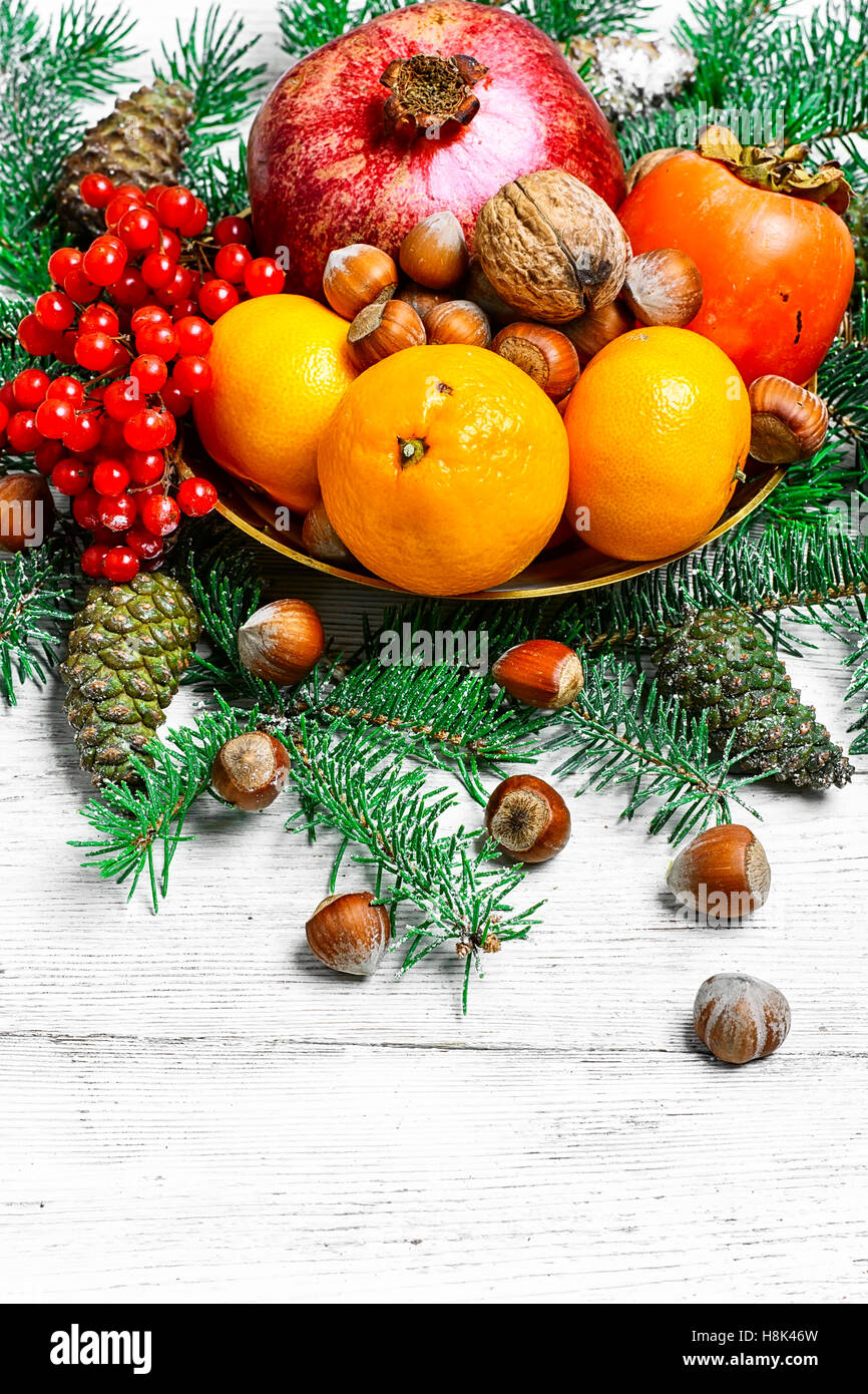 dish with tangerines,pomegranates,persimmons and nuts,decorated with fir branches Stock Photo