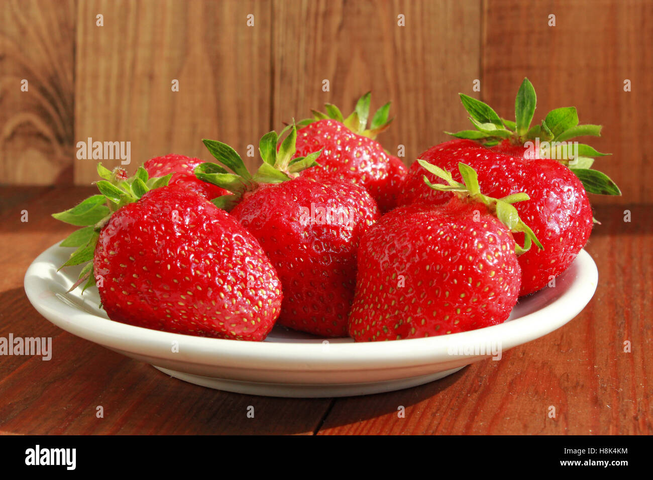 ripe red strawberries on the white plate on the brown background Stock Photo