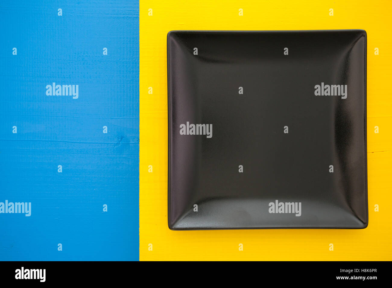 Empty black ceramic dish on over blue and yellow wooden table, square ...