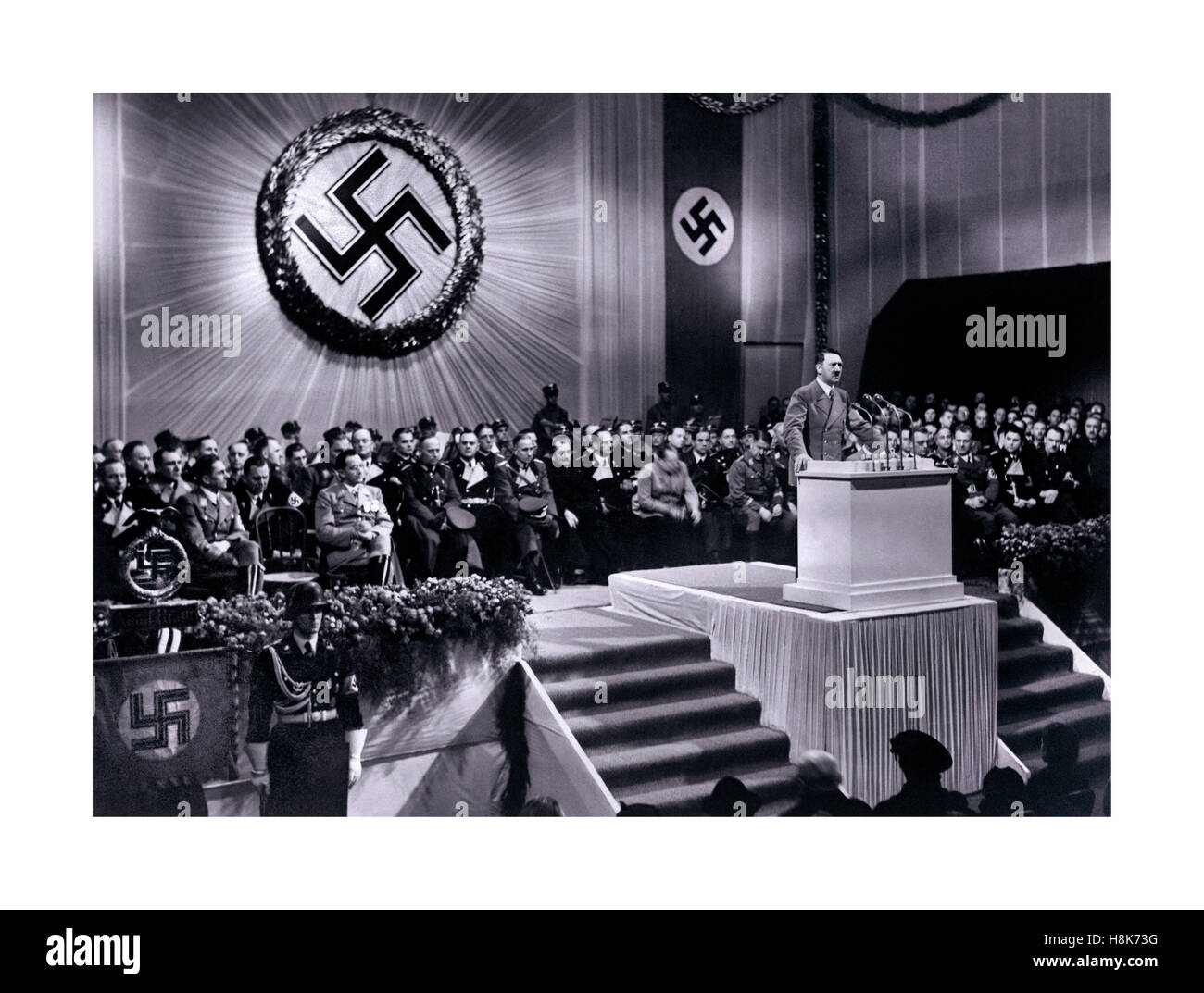 Adolf Hitler Speech, 1939 speaking under a large shining swastika emblem at a podium speech meeting with other ranking Nazi party supporters 1939 Berlin Germany Stock Photo
