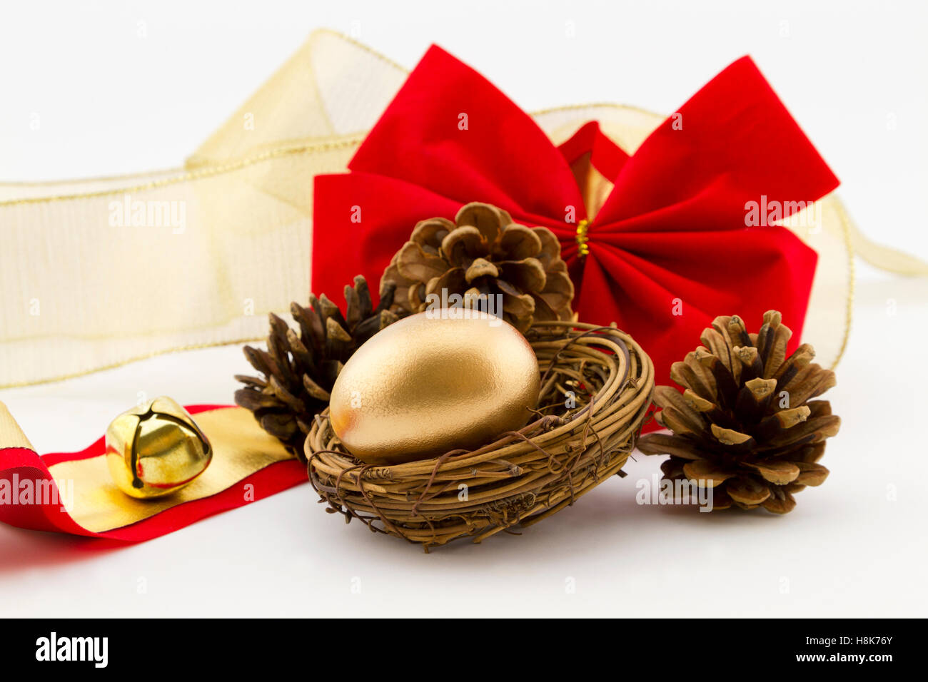 Gold nest egg surrounded by pine cones placed with red velvet bow and gold bell and ribbon.  Holiday financial gift is festive. Stock Photo