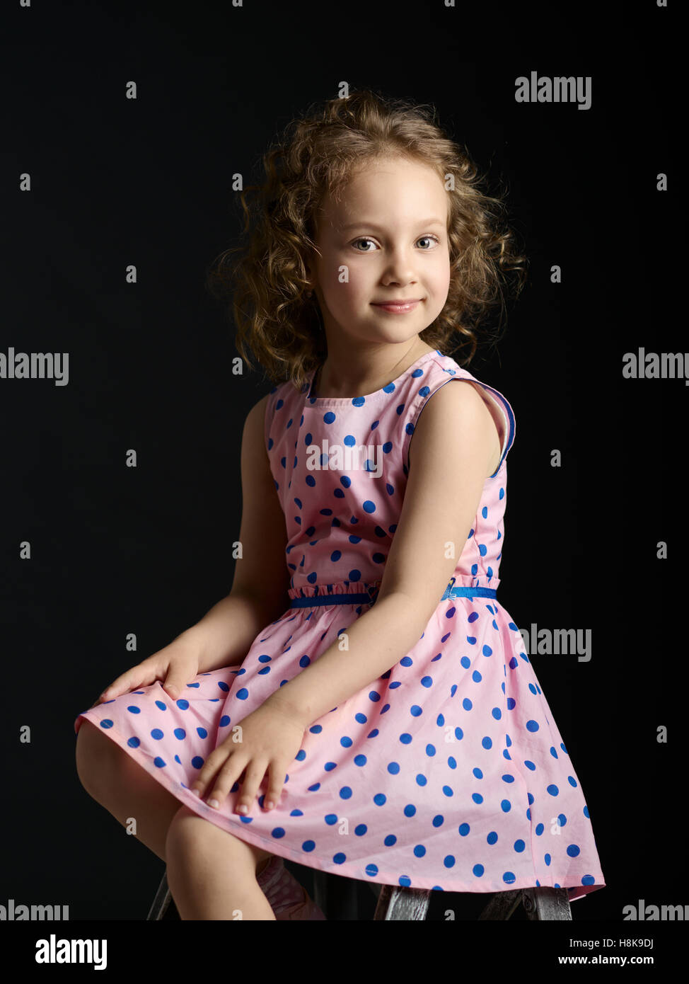 Classic portrait of a little girl in a pink dress with a smile on dark ...