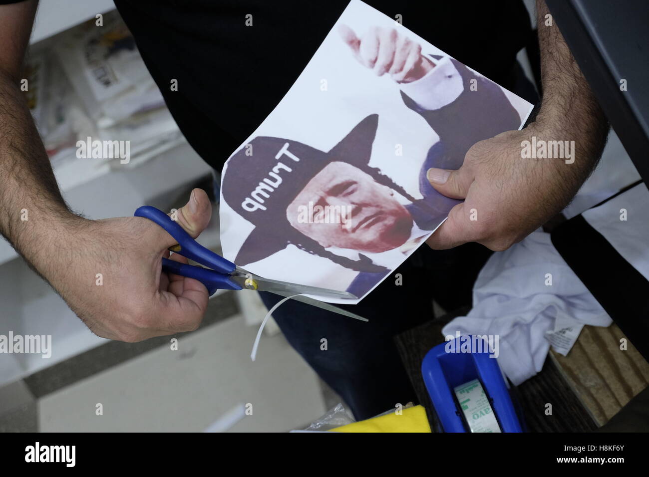 Jerusalem, Israel. 13th  NOV, 2016. A Palestinian man cutting a paper depicting newly elected US President Donald Trump dressed to look like an ultra-orthodox Jew in order to prepare a T-shirt bearing this image at a souvenir shop in the old city East Jerusalem, Israel on 13 November 2016. Stock Photo