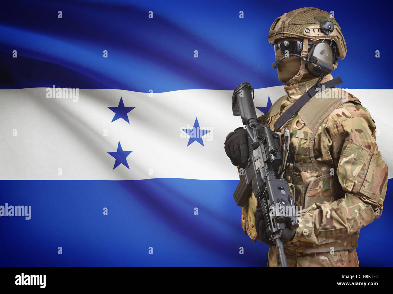 Soldier in helmet holding machine gun with national flag on background - Honduras Stock Photo