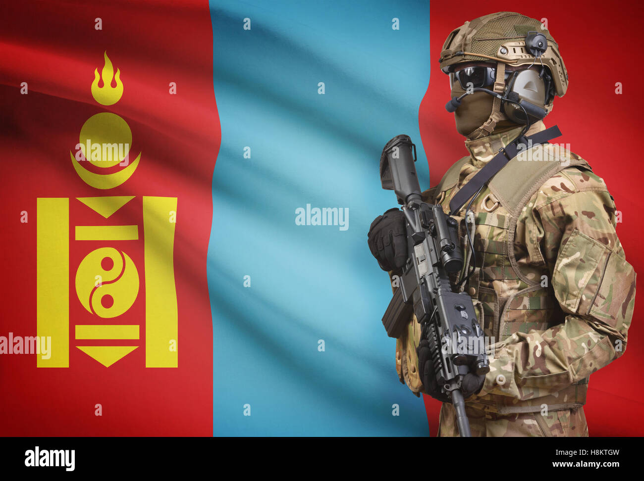 Soldier in helmet holding machine gun with national flag on background - Mongolia Stock Photo