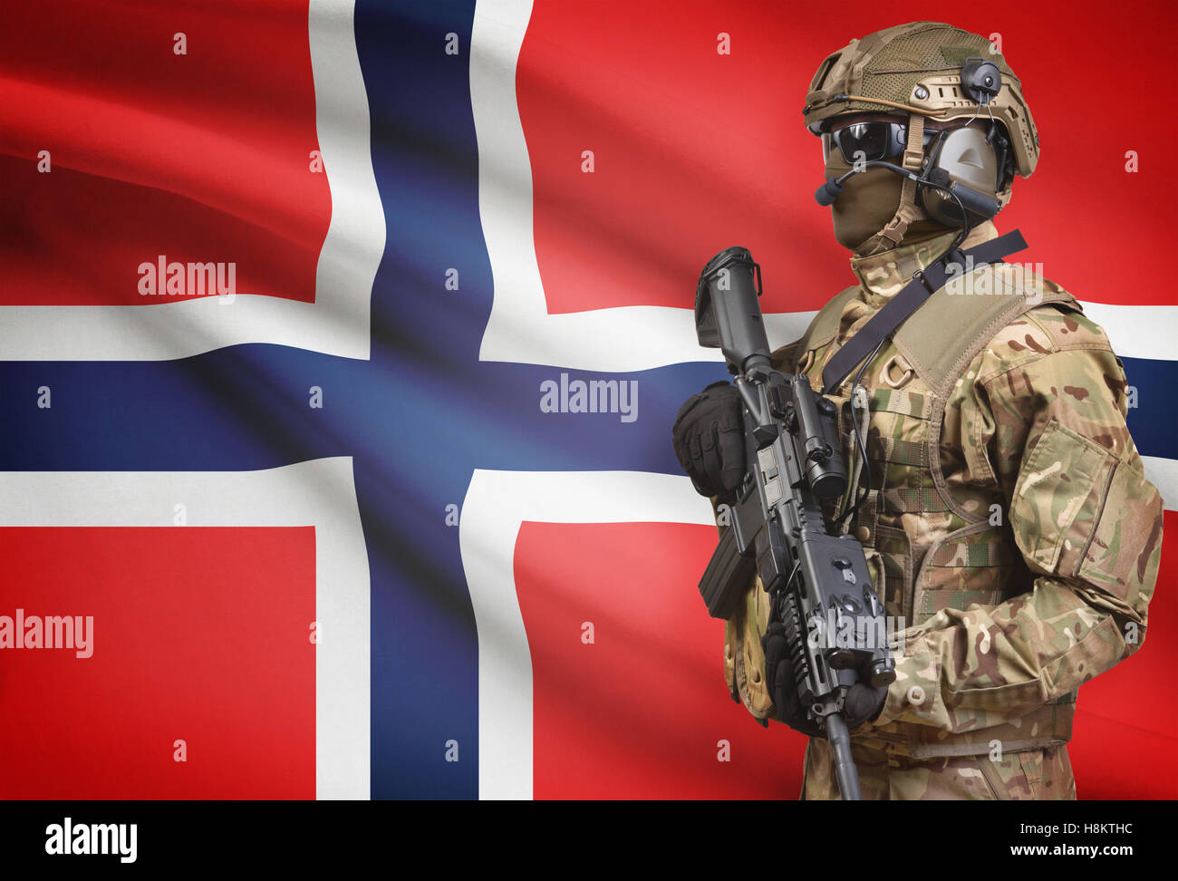 Soldier in helmet holding machine gun with national flag on background - Norway Stock Photo