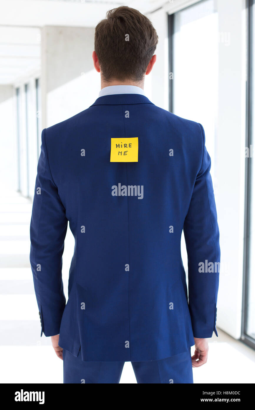 Rear view of young businessman with hire me adhesive note at office Stock Photo