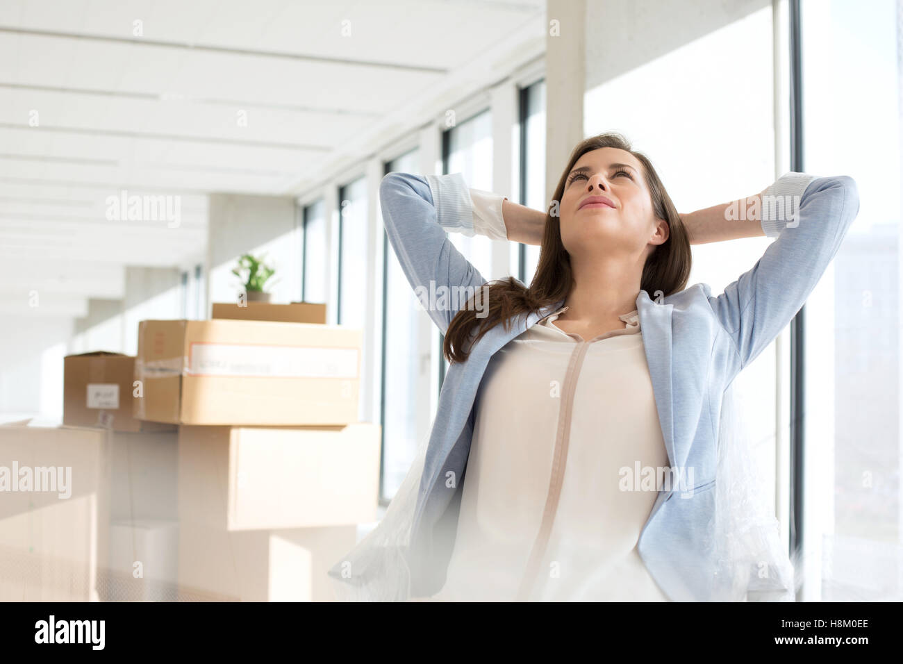 Thoughtful young businesswoman with hands behind head in new office Stock Photo