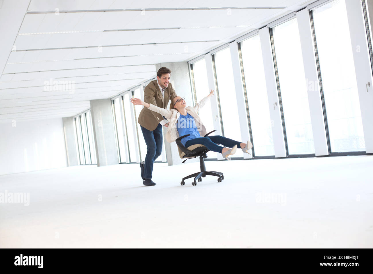 Young businessman pushing female colleague in chair at empty office Stock Photo
