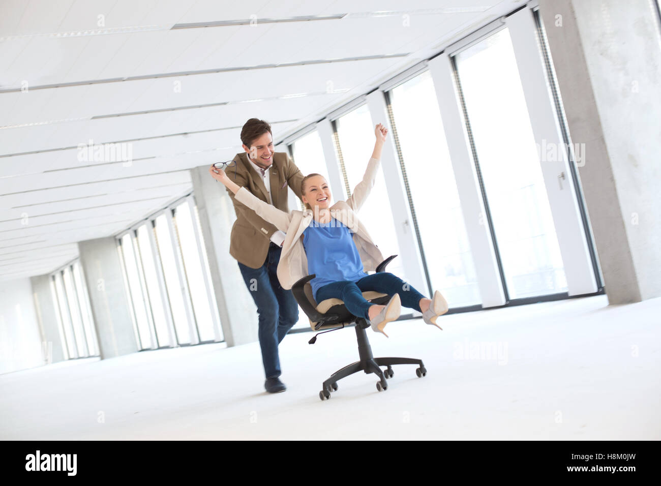 Full length of young businessman pushing female colleague in chair at empty office Stock Photo