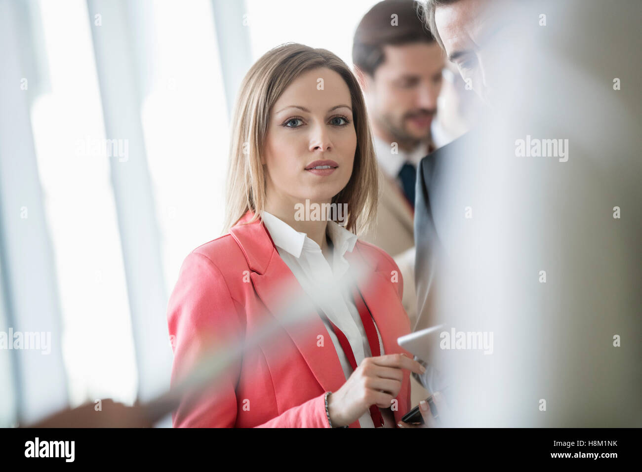 Portrait of confident businesswoman standing with colleagues in brightly lit convention center Stock Photo