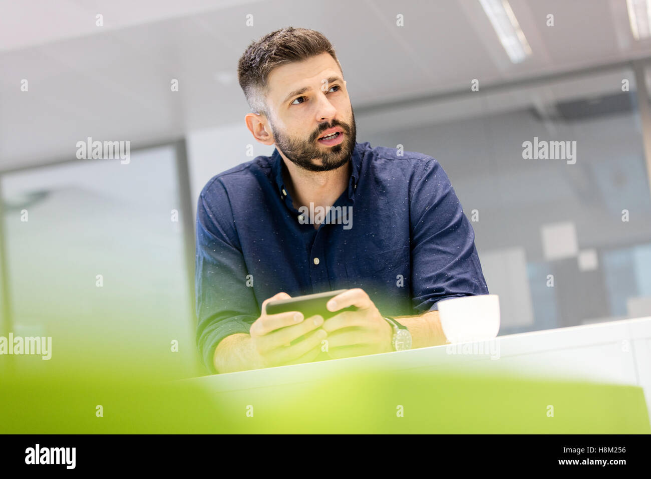 Mid adult businessman holding smartphone while looking away in office Stock Photo