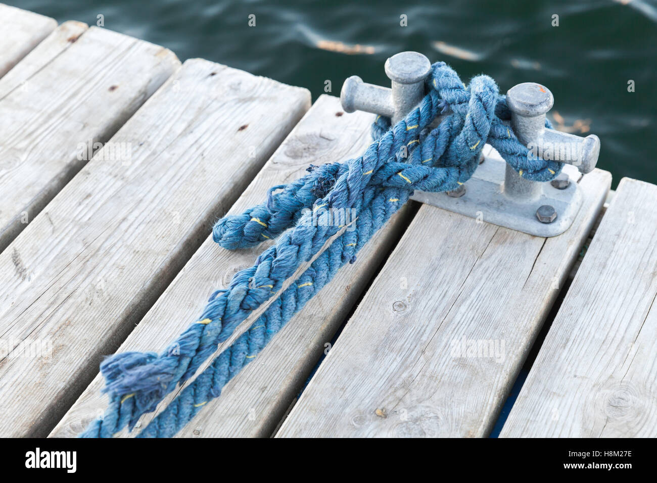 Mooring bollard with tied blue nautical rope mounted on white wooden pier, yacht marina safety equipment Stock Photo