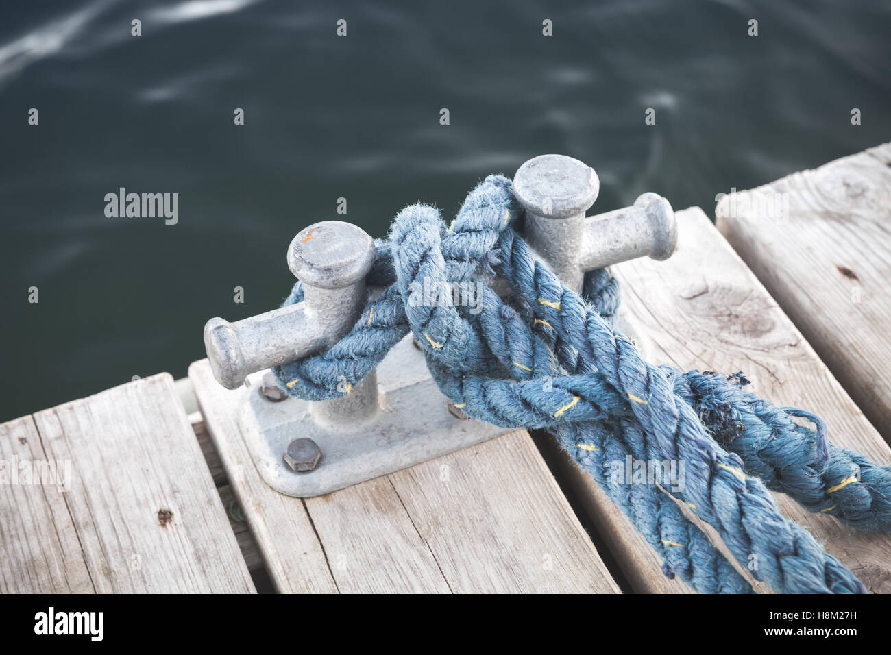 Mooring bollard with tied blue rope mounted on white wooden pier, yacht marina safety equipment Stock Photo