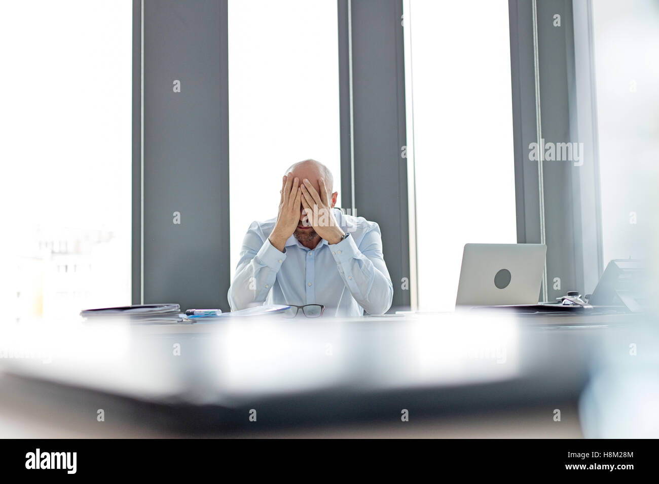 Tired mid adult businessman covering face at desk in office Stock Photo