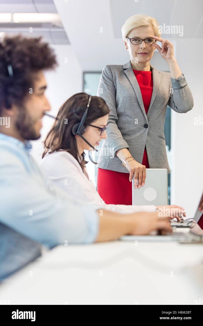 Portrait of confident mature businesswoman with operators working at desk in office Stock Photo