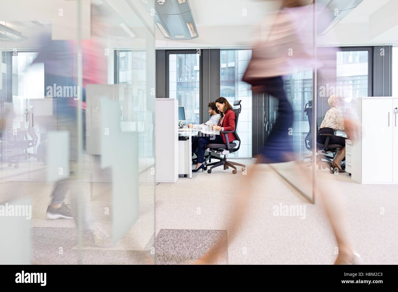 Blurred motion of businesswoman walking with colleagues working in background at office Stock Photo