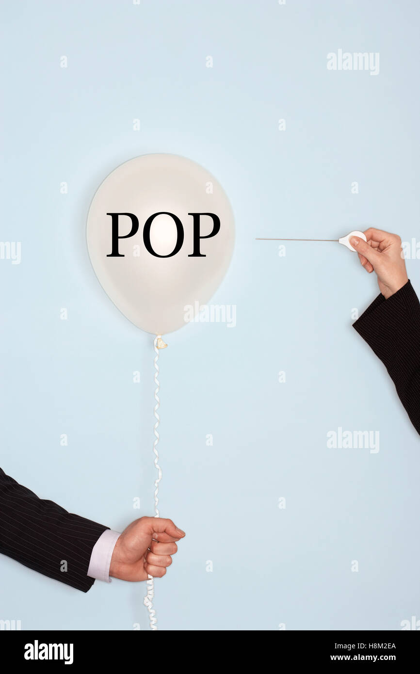 Cropped hands holding needle and popping balloon with text saying POP Stock Photo