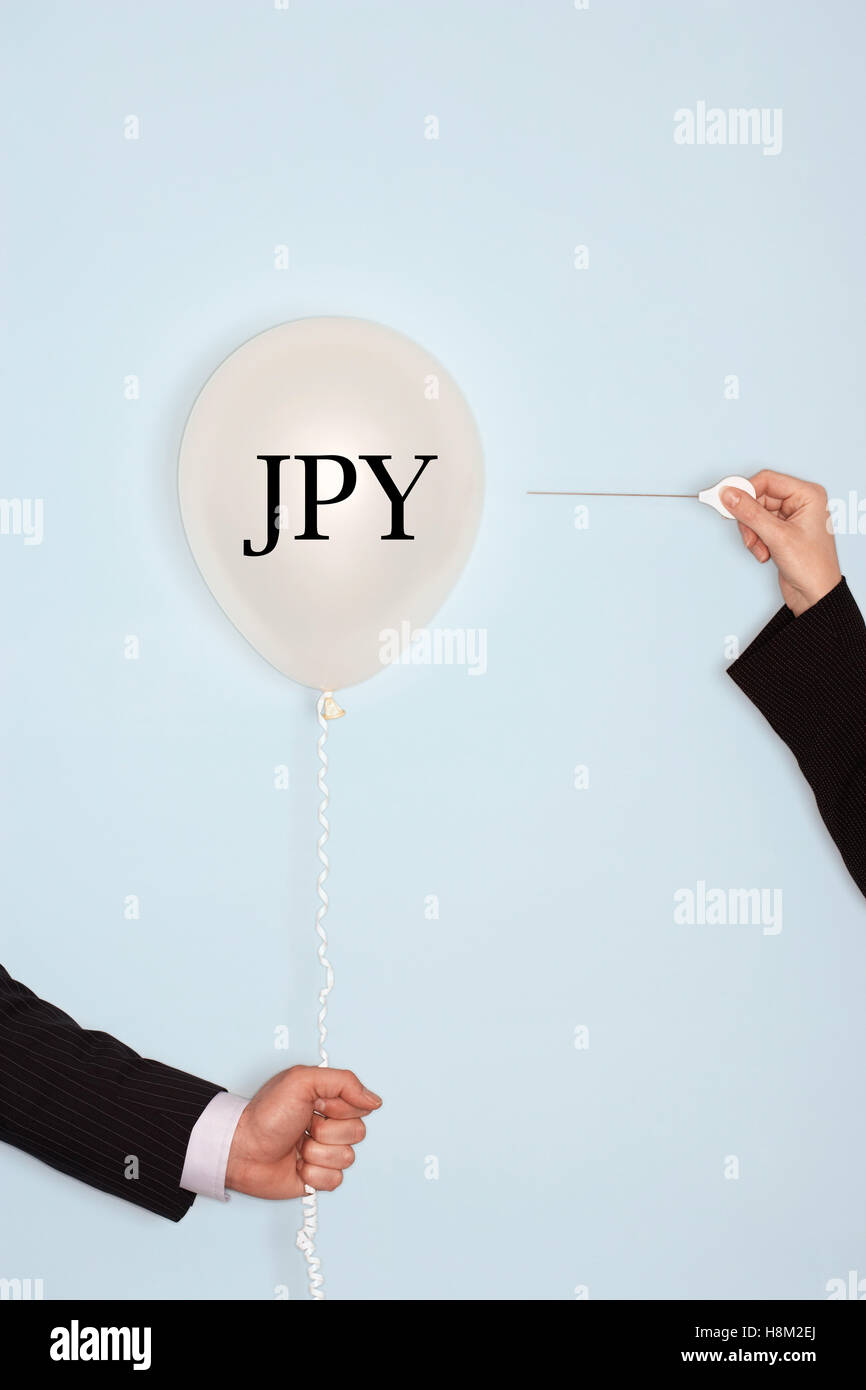 Cropped hands holding needle and popping balloon with JPY written in text Stock Photo