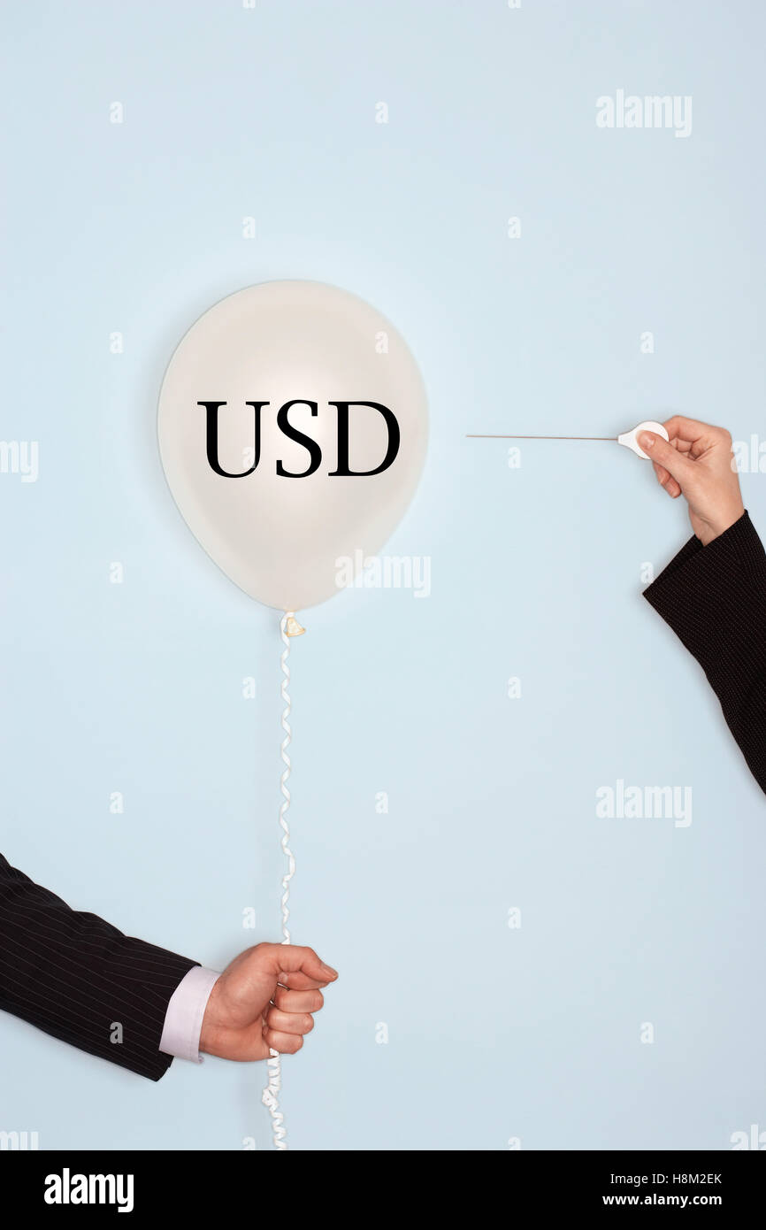 Cropped hands holding needle and popping balloon with text saying USD Stock Photo