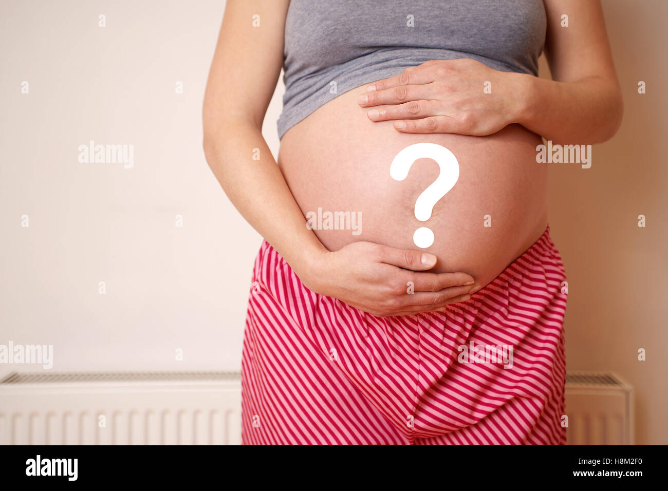 Midsection of an expectant woman touching belly while standing against wall Stock Photo