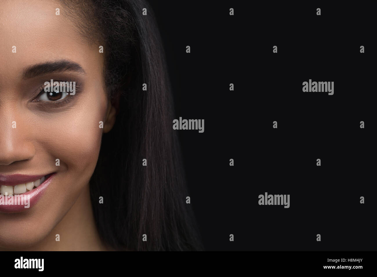 Half-face portrait of beautiful smiling sensitive afro american woman on dark background Stock Photo