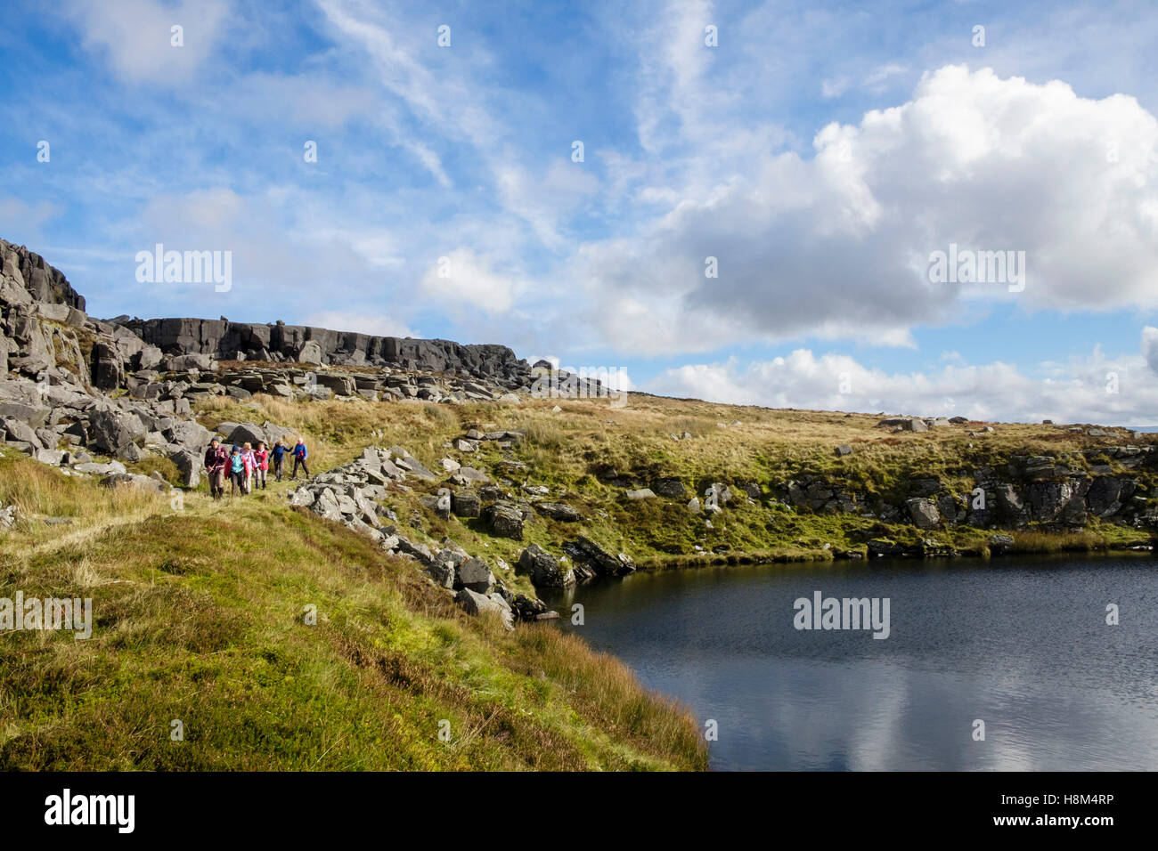 Hikers hiking by a small upland lake in Rhinog mountains of southern ...