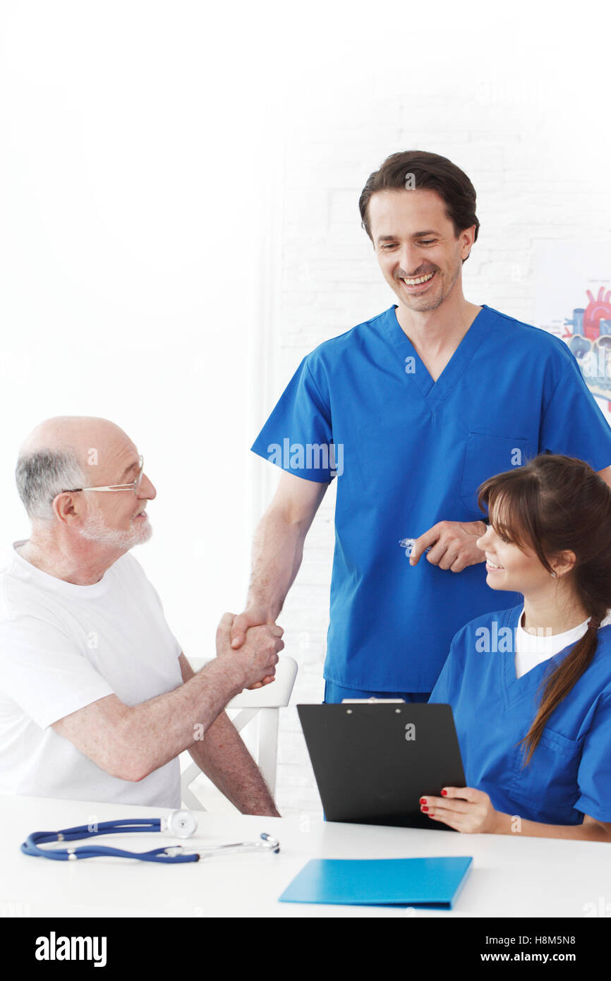 Happy senior patient and doctors in hospital shaking hands Stock Photo