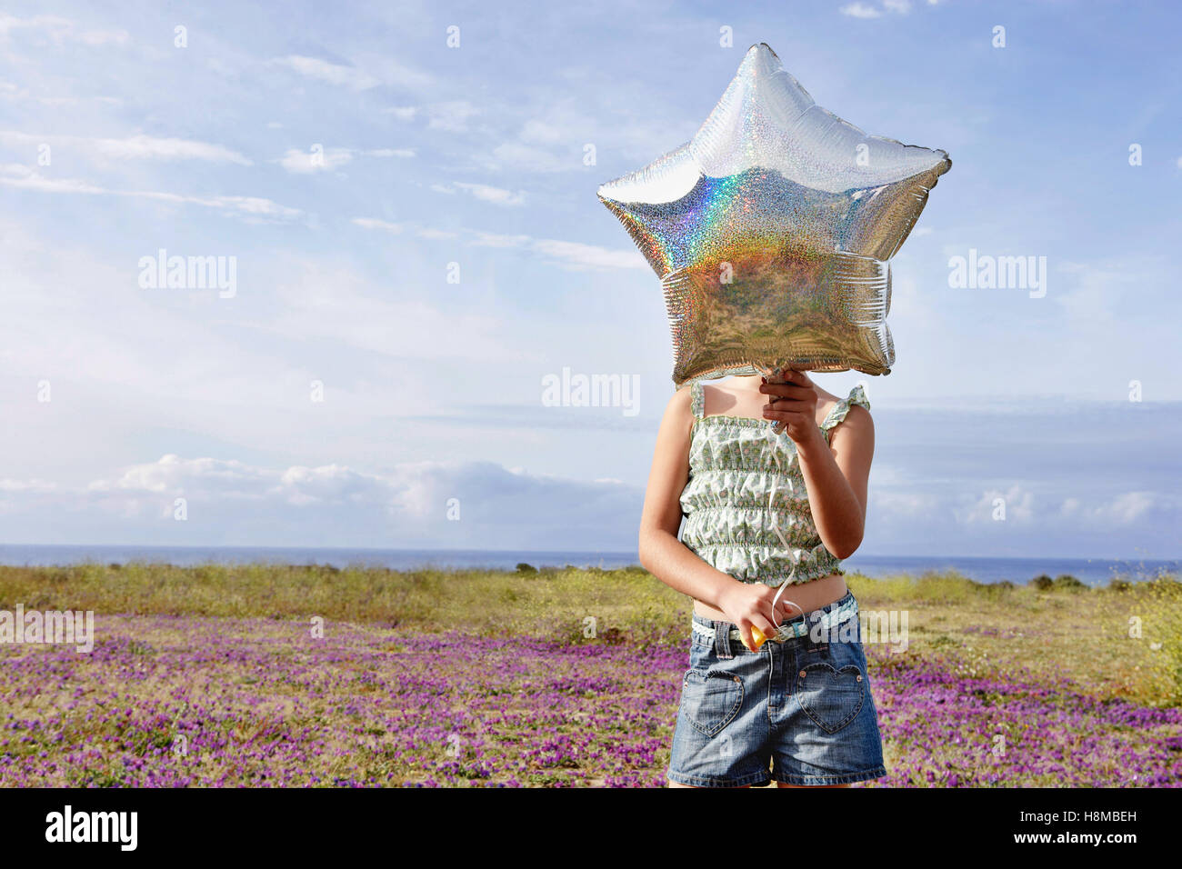 Front view of preadolescent girl holding star shaped balloon in front of her face while standing at flower field Stock Photo