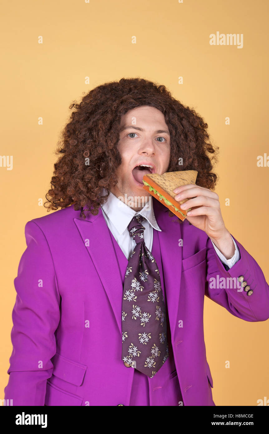 Caucasian man with afro wearing Purple Suit eating sandwich Stock Photo