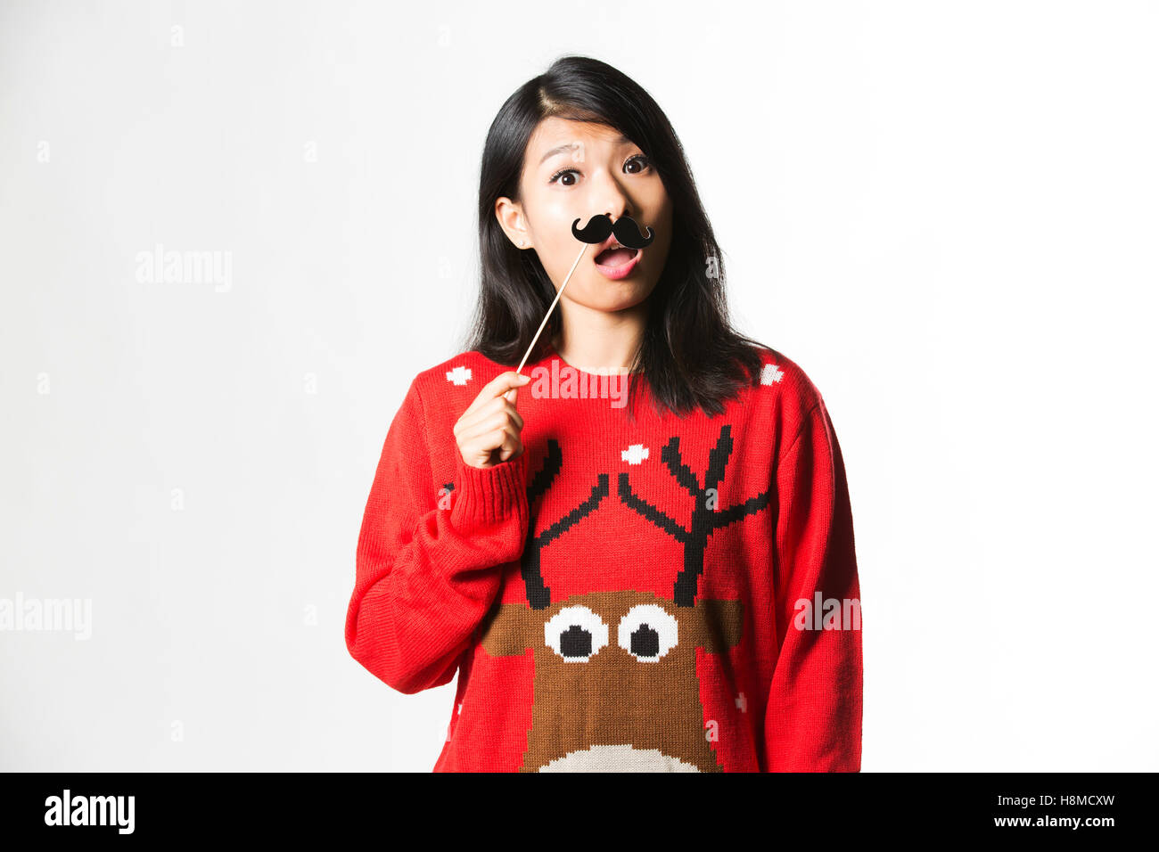 Portrait of woman in Christmas sweater standing with fake moustache Stock Photo