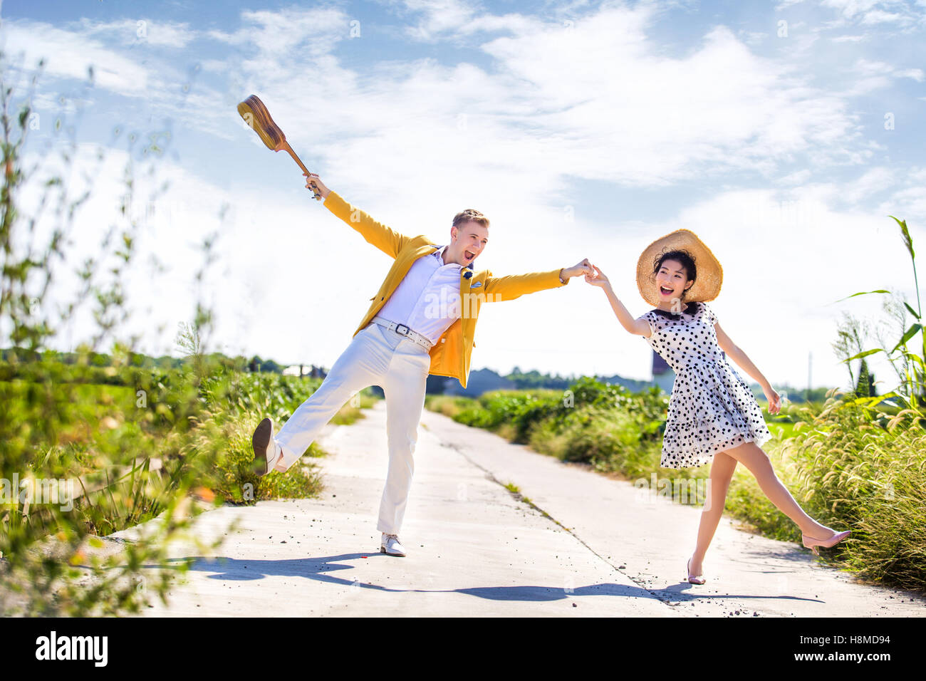 Full length of playful couple on footpath amidst field on sunny day Stock Photo