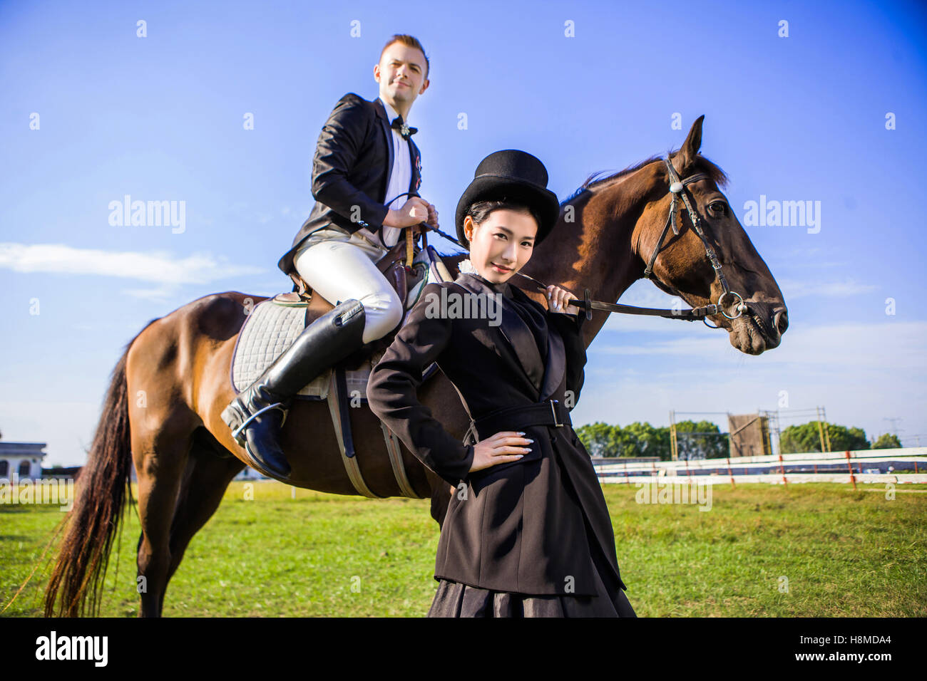 Portrait of confident woman standing by man sitting on horse at field Stock Photo