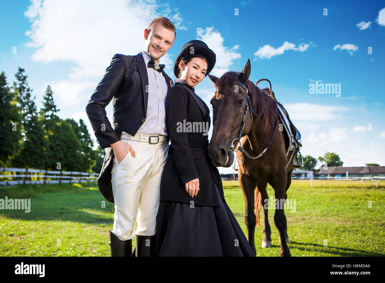 Portrait of confident well-dressed couple standing with horse on field Stock Photo
