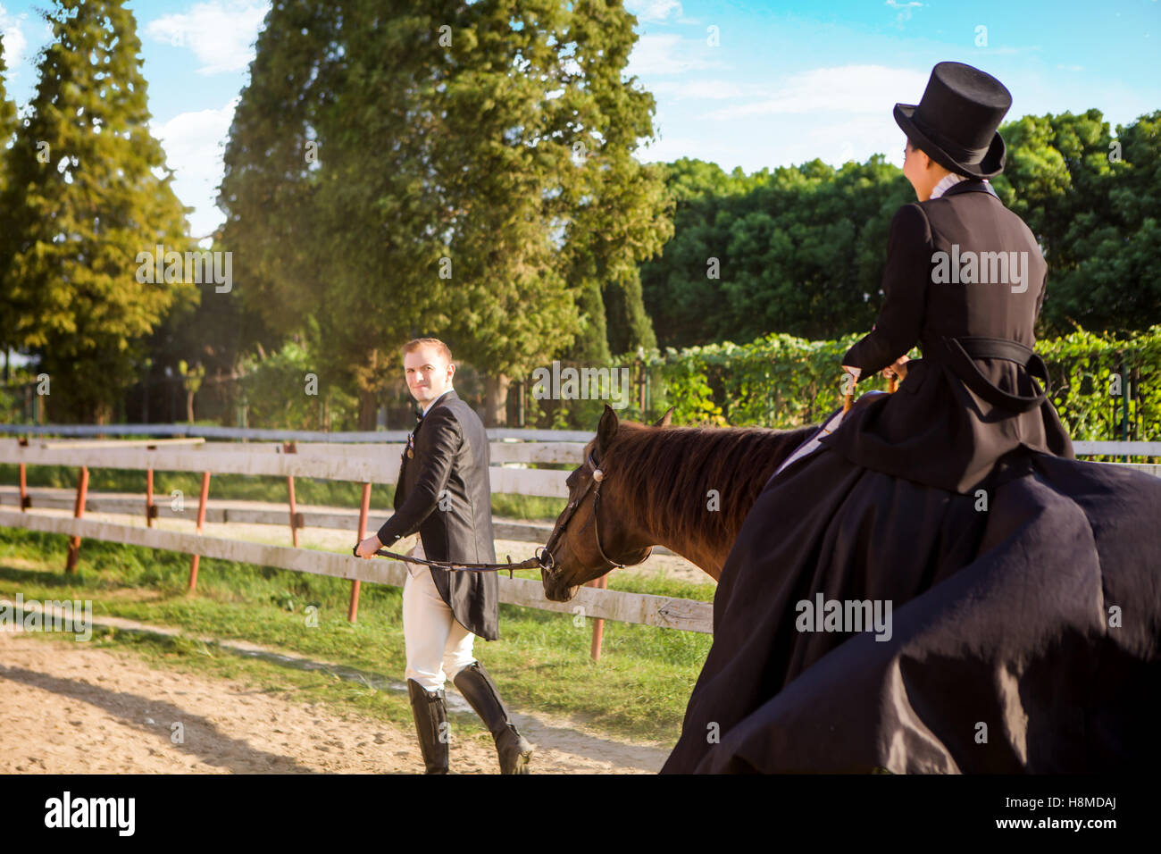 Well-dressed man pulling woman sitting on horse at field Stock Photo